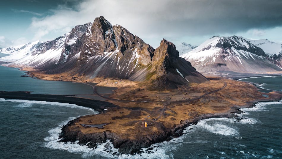 An aerial view of a narrow peninsula with dramatic snow-capped mountains
