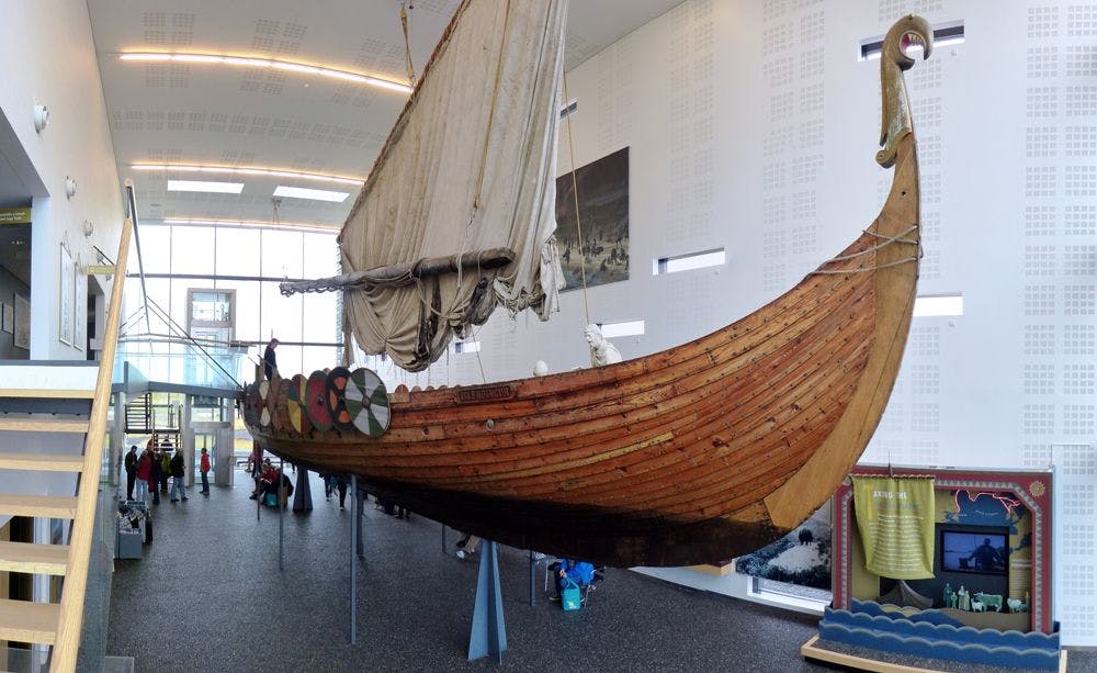 A Viking longship, with an upwards curving stern and prow with a carved dragonhead and a centrally positioned square sail.