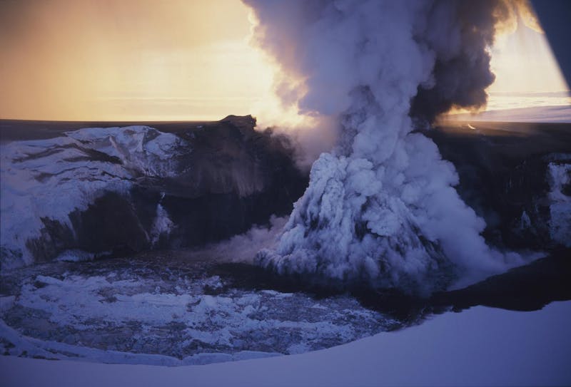 Black ash and steam rising from an ice-covered crater lake