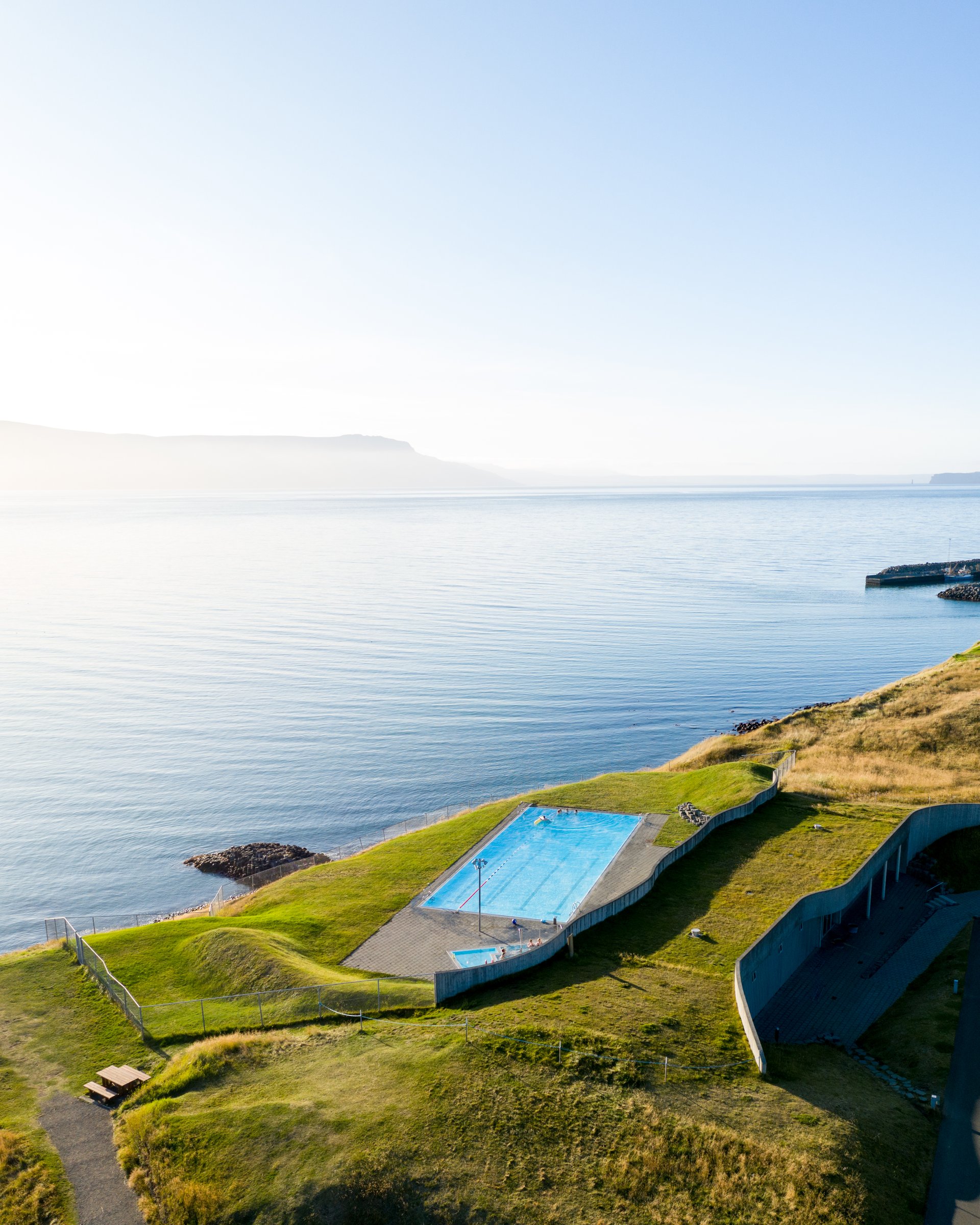 Bird's eye view of a swimming pool situated on the cliffs by the ocean, the sun is shining