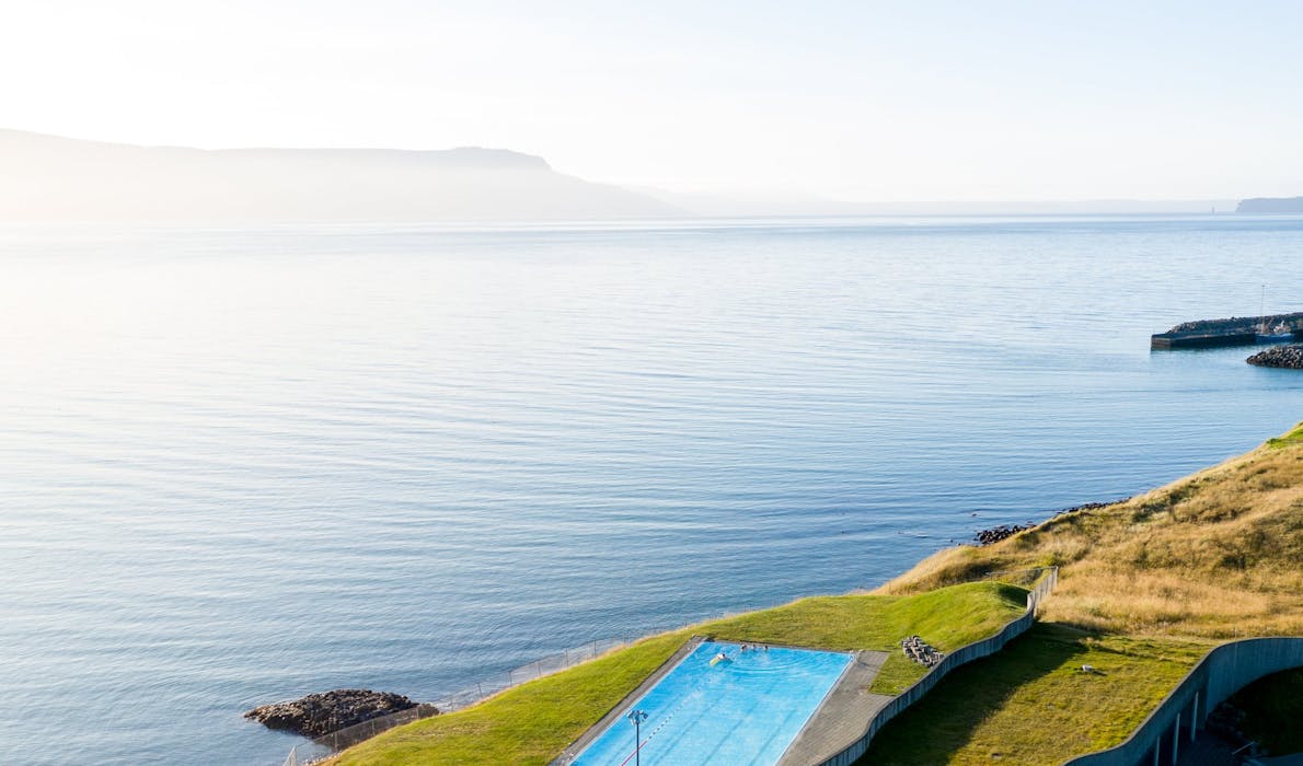 Birdview of a swimming pool situated on the cliffs by the ocean, the sun is shining