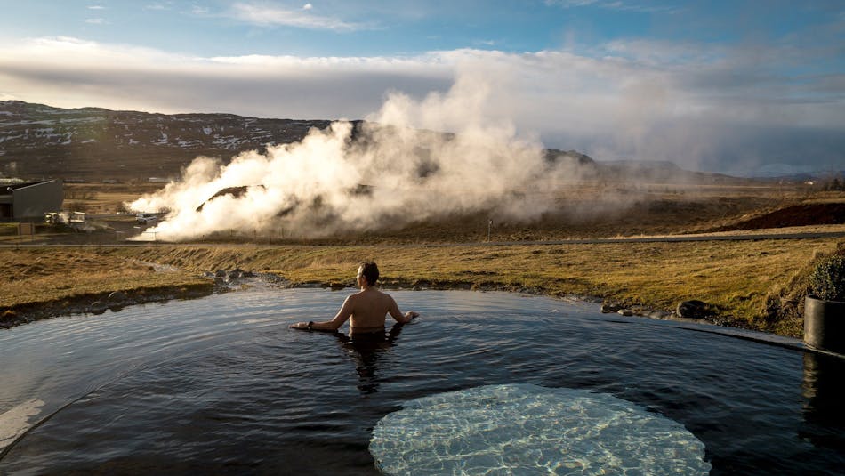 Man in a pool of Krauma geothermal baths watching the hot water steam from Deildartunguhver below