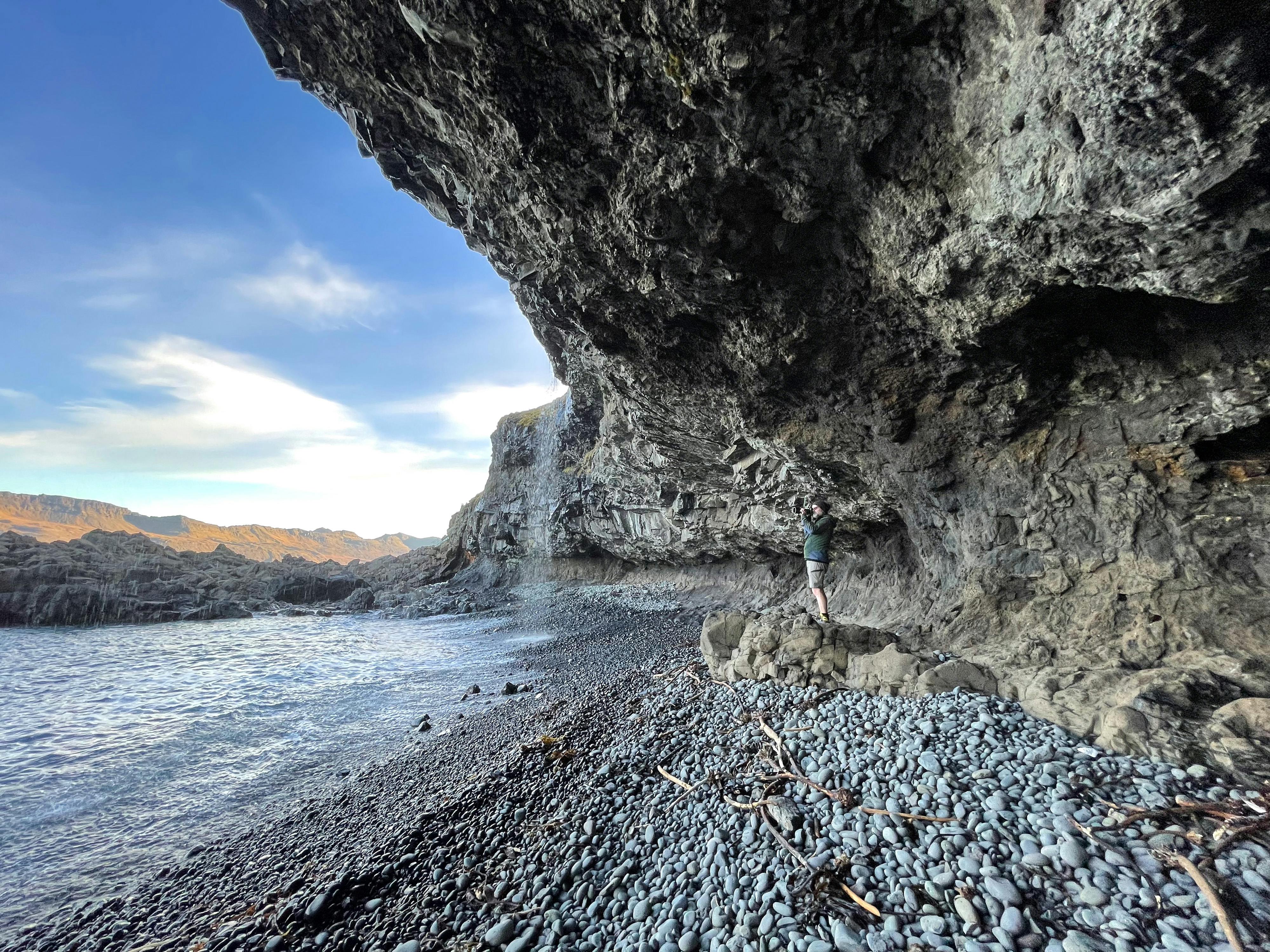 A man standing in a sea cave near a small waterfall