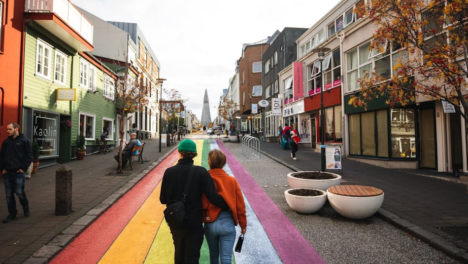 A couple walks up the rainbow street on Skolavörðustígur in Reykjavík towards Hallgrimskirkja