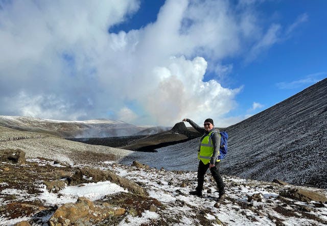 A person pointing at a small erupting crater in the backdrop