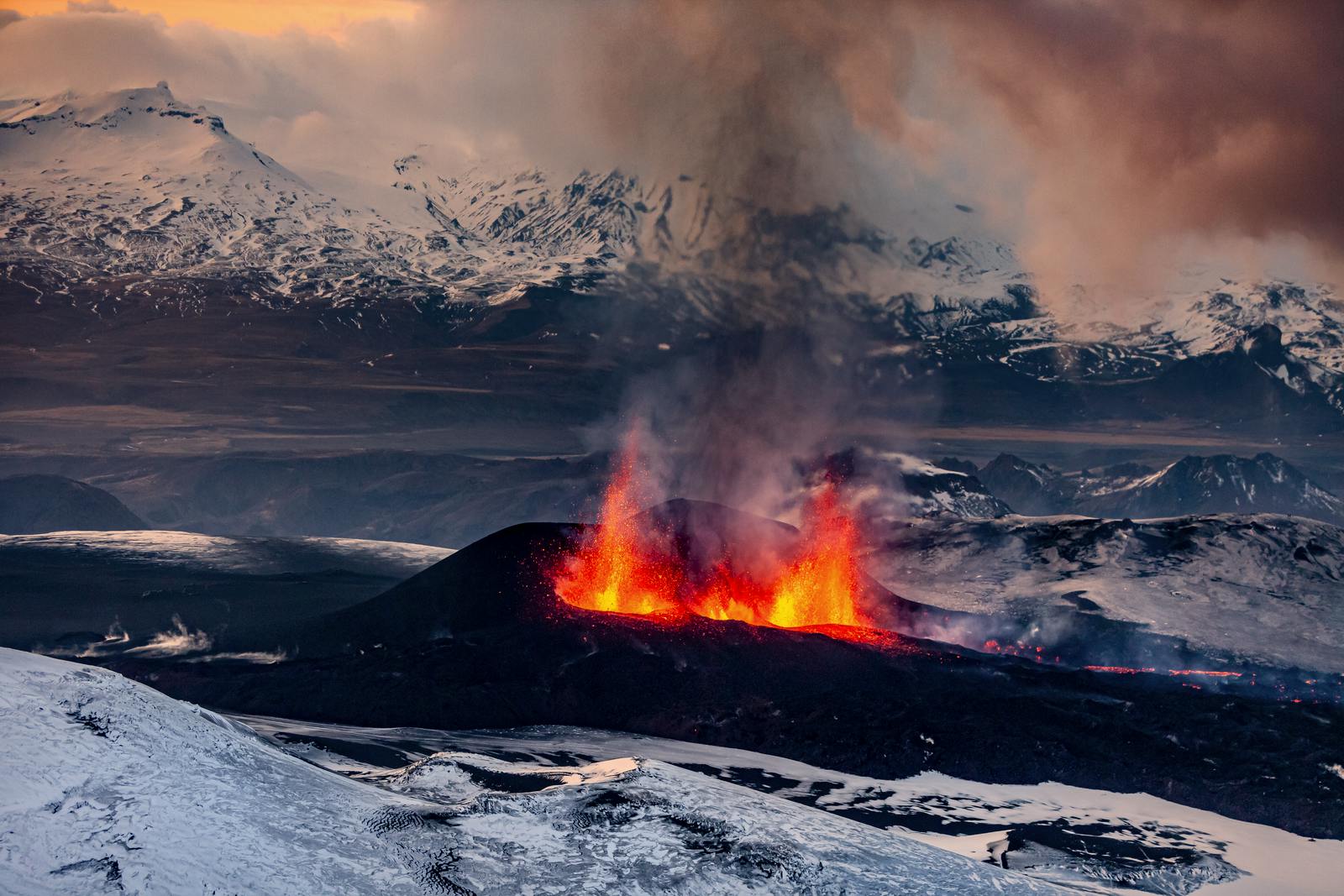 Fire fountains from two erupting craters, enveloped by snowy mountains