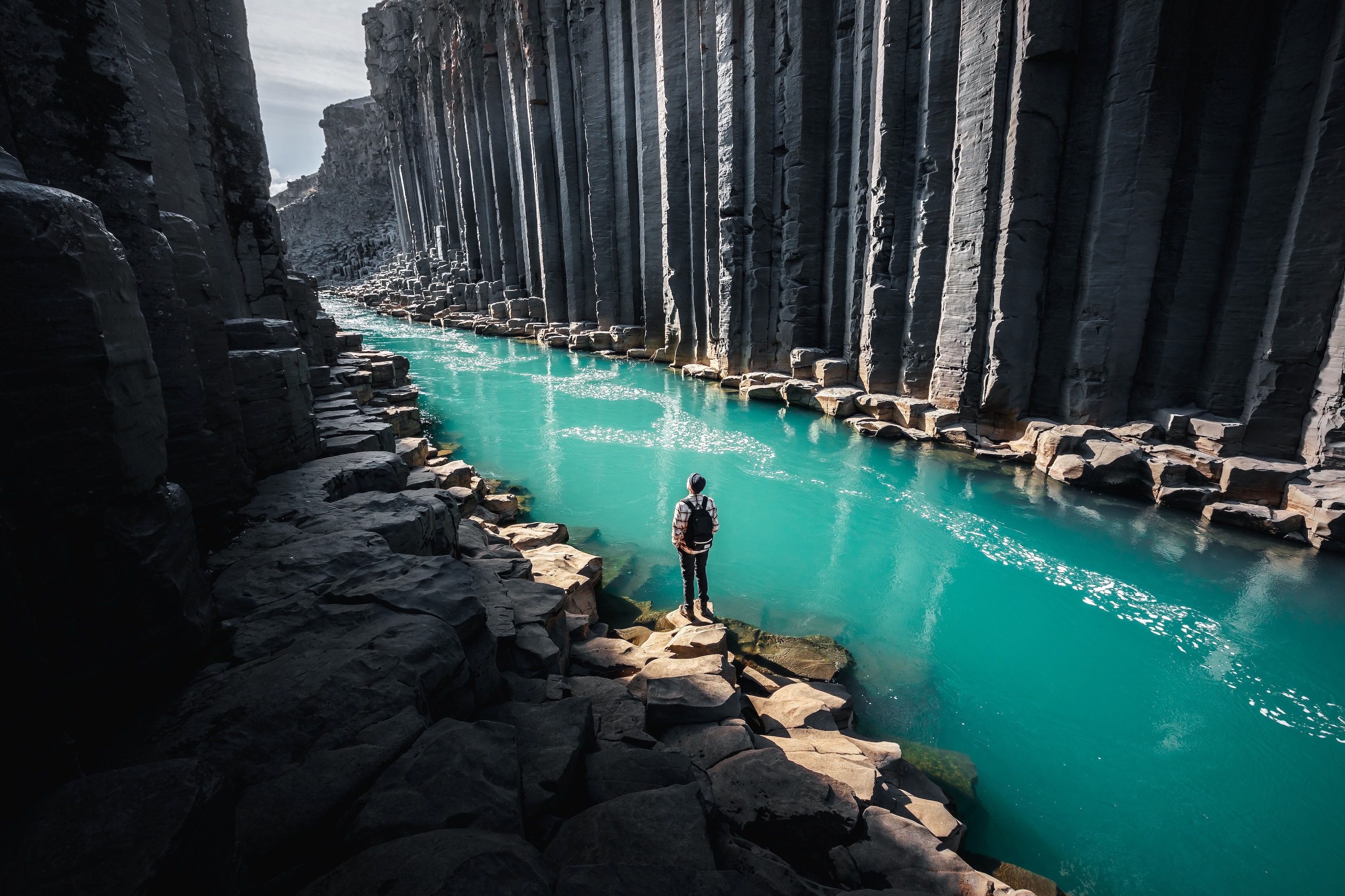 A man standing in a gorge with green river and giant basalt column walls