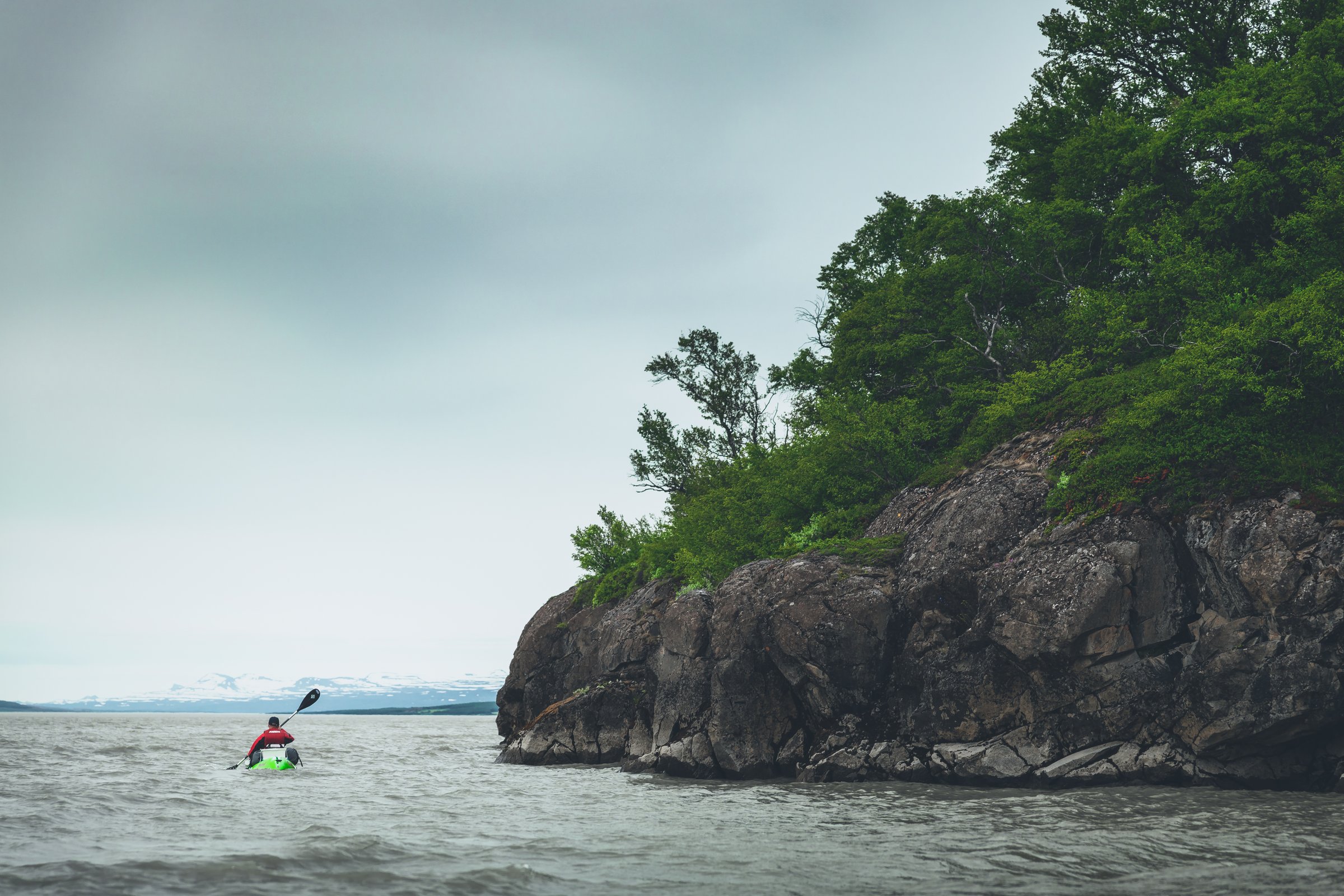 Man kayaking on a river along a cliff with trees on top
