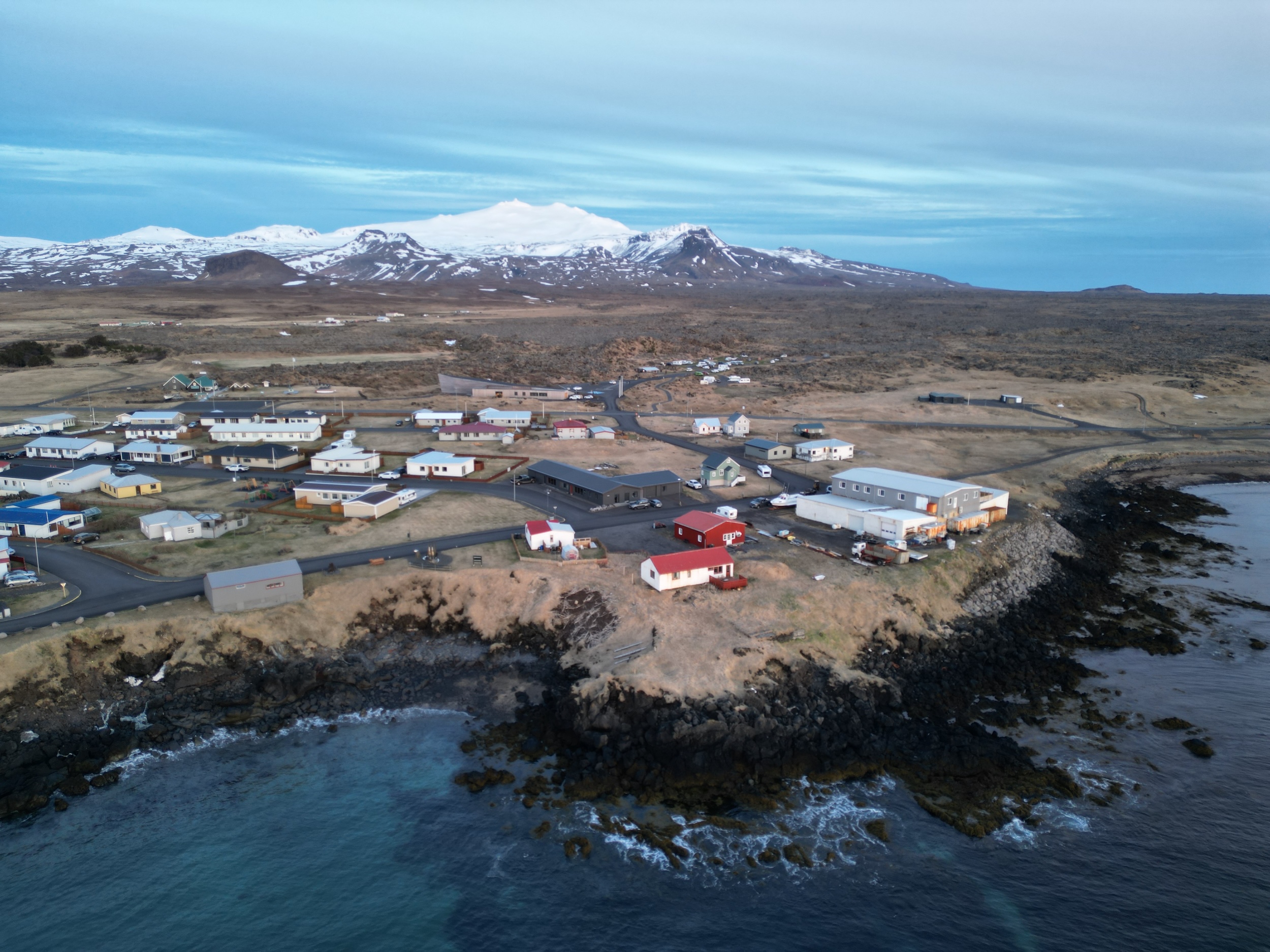 A small village in on a rugged beach with a volcano and glacier in the backdrop
