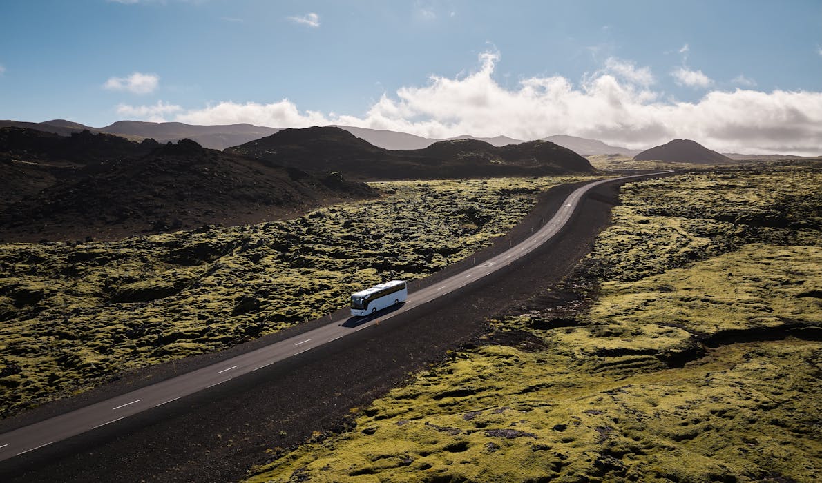 Bird's eye view of a white tour bus in the mossy green landscape of Iceland.