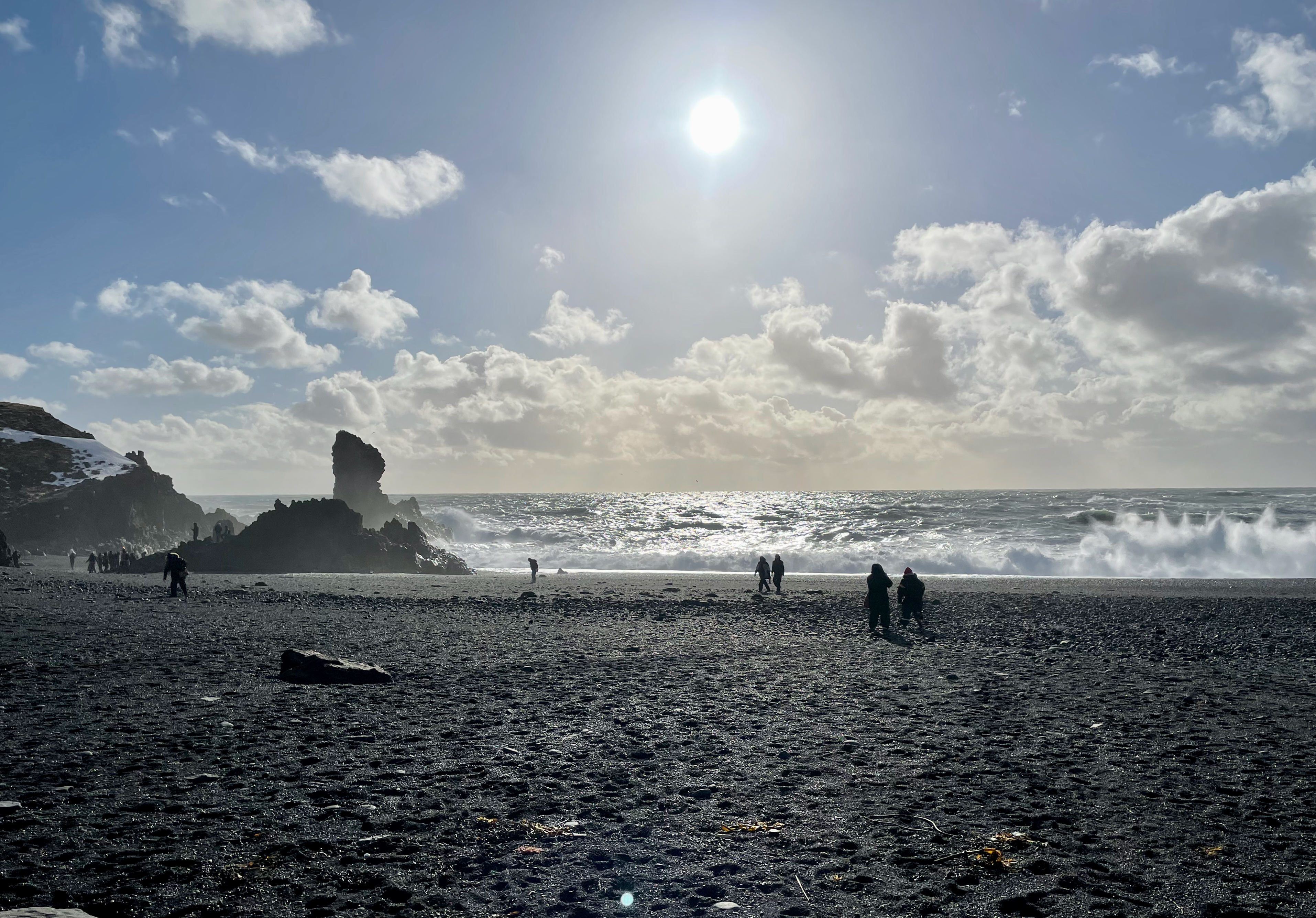 people walking on black sand beach with crashing waves