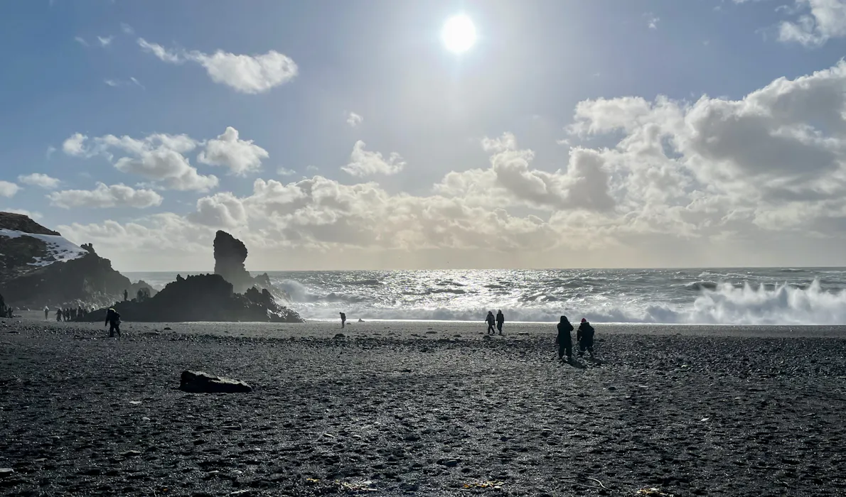 people walking on black sand beach with crashing waves