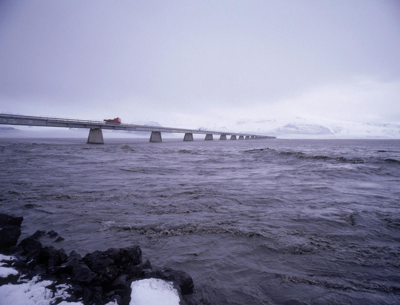 A wast and muddy river flowing under a long bridge in a jokulhlaup