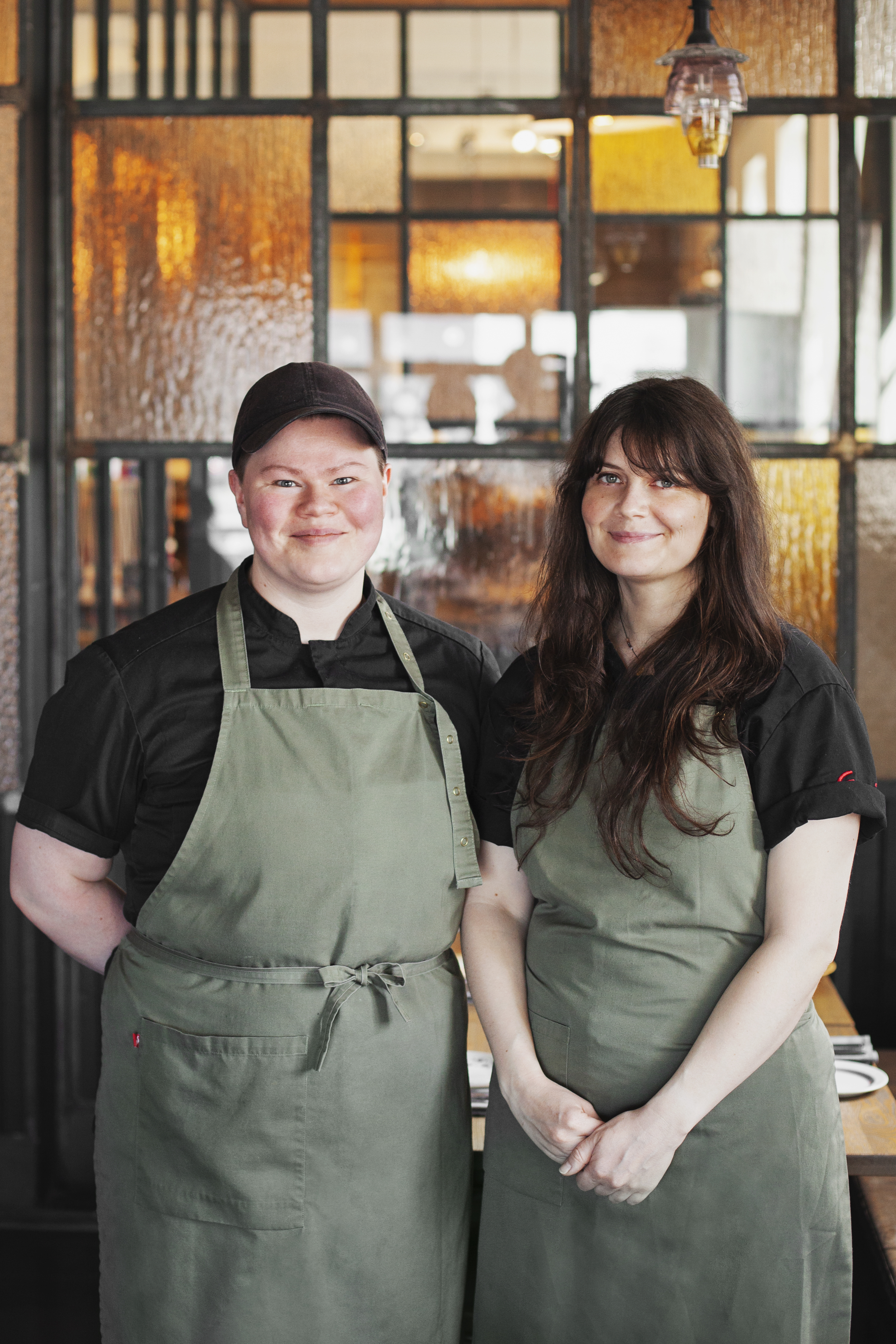 Chefs Helga and Wiola of Matur og Drykkur stand side by side in the restaurant, wearing aprons and smiling, known for their modern take on traditional Icelandic cuisine.