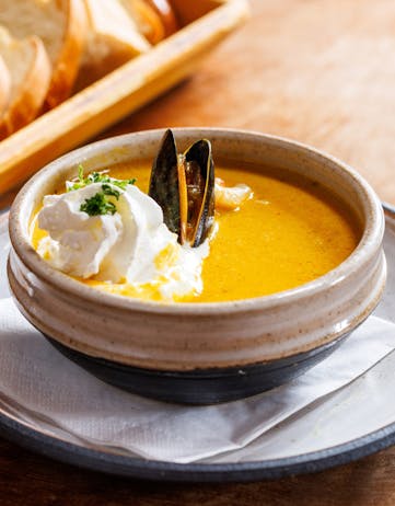 A yellow fish soup in a bowl with cream on top