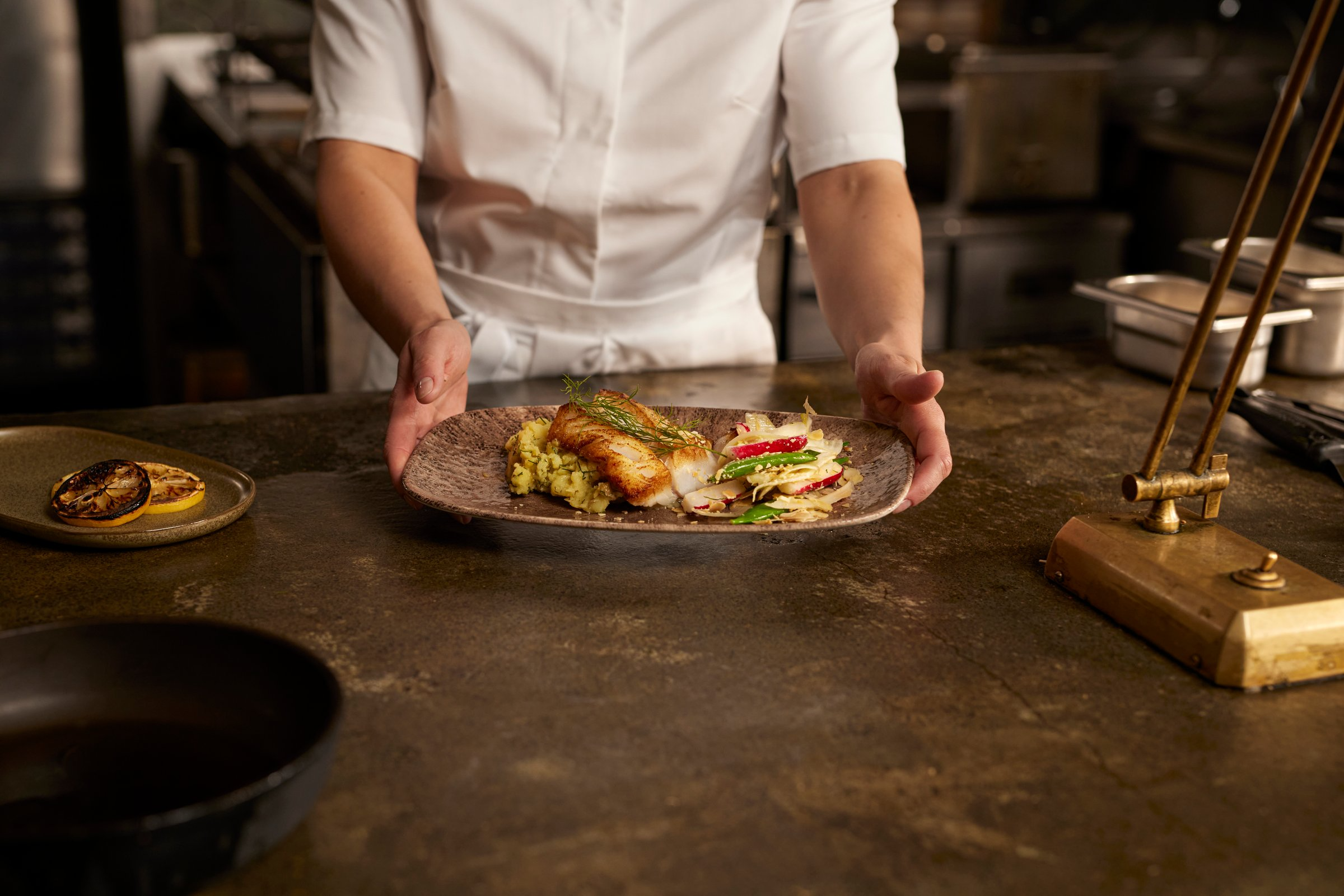 Chef serving a plated Icelandic cod dish with vegetables and garnish.