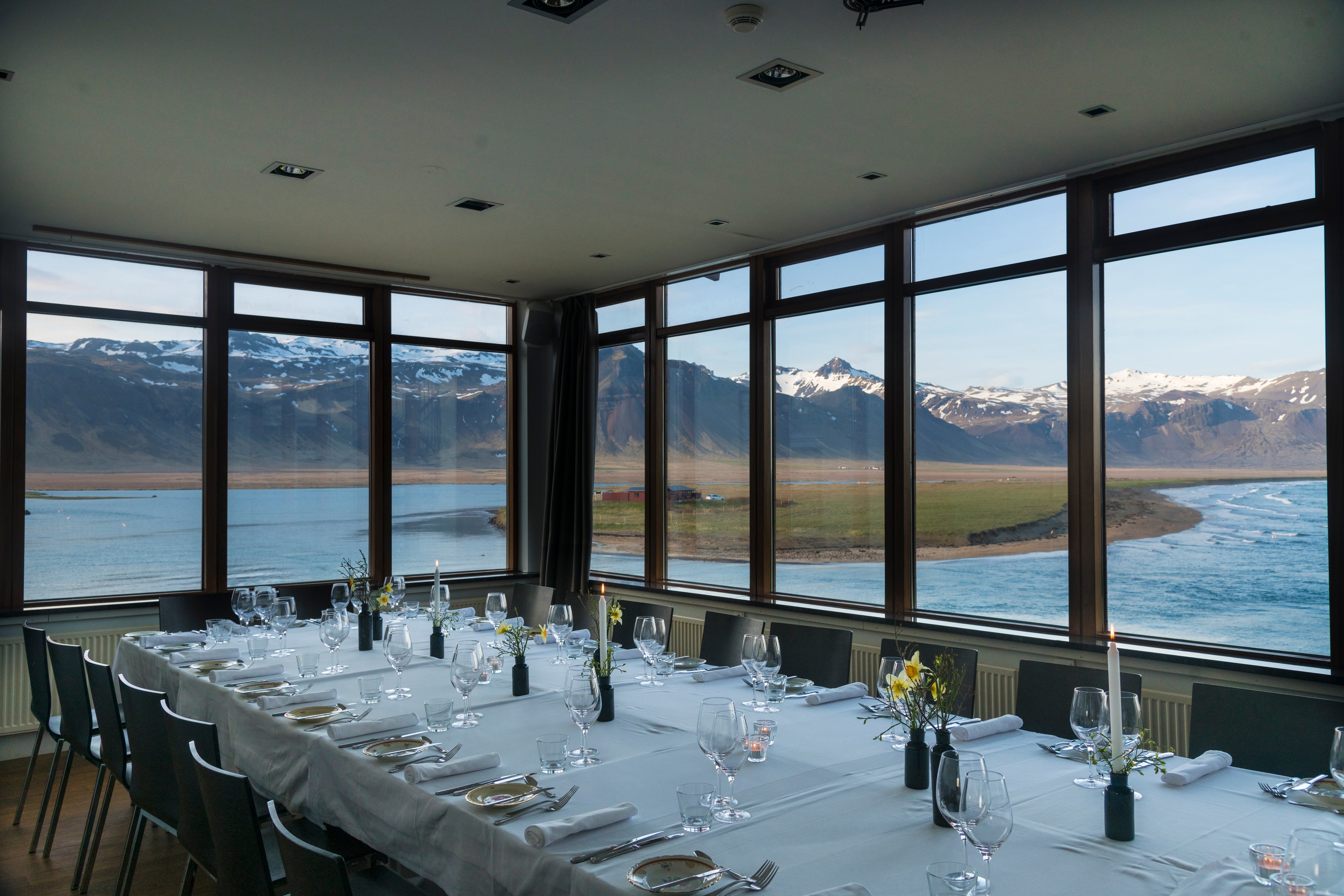Elegant dining table set by large windows with mountain and ocean views in Iceland.