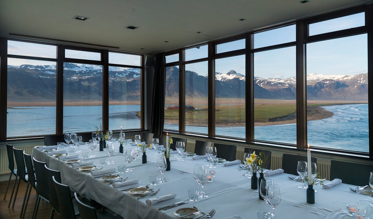 Elegant dining table set by large windows with mountain and ocean views in Iceland.