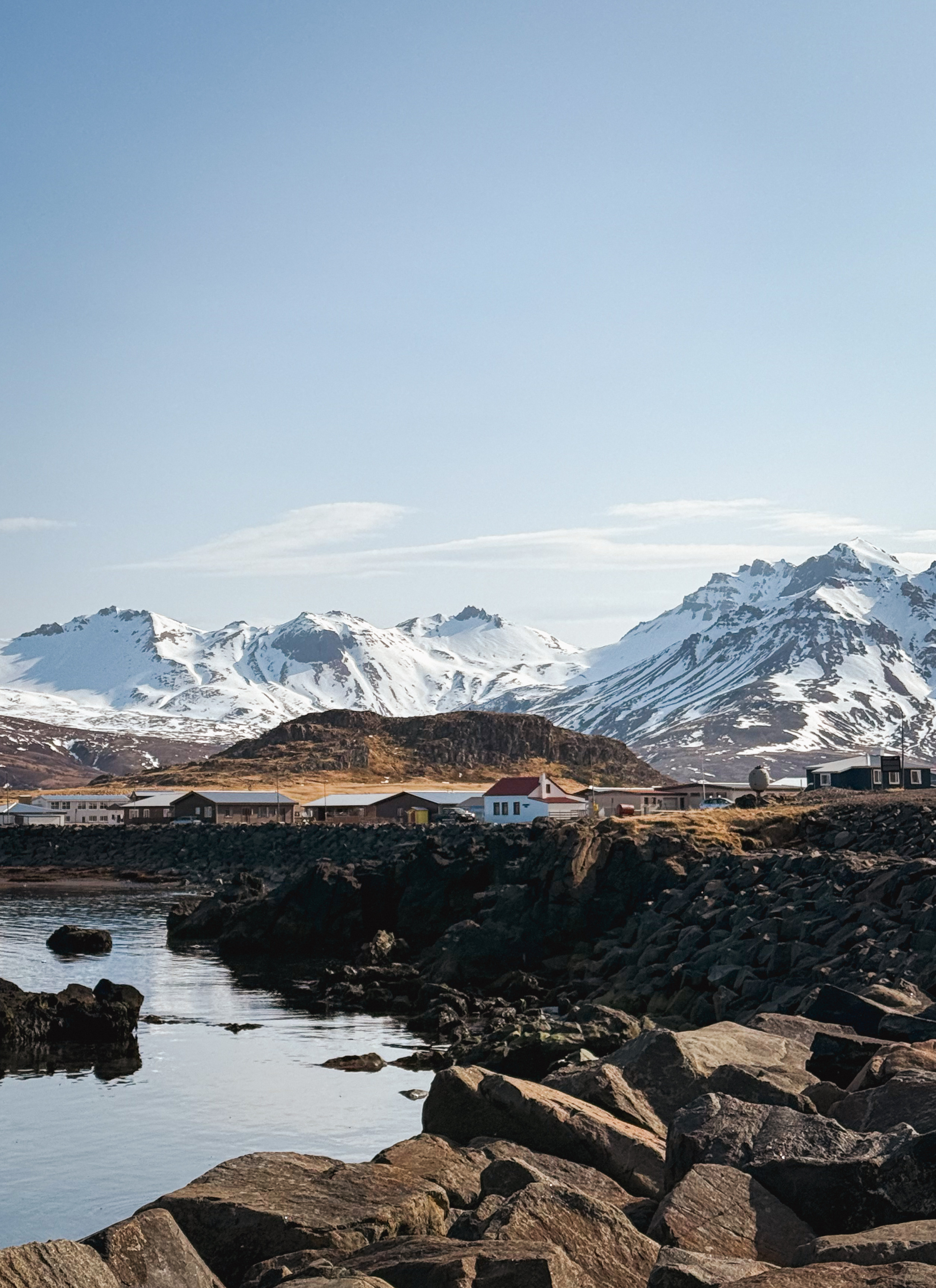 A white house with a red roof and mountains behind it, in Borgarfjörður Eystri.