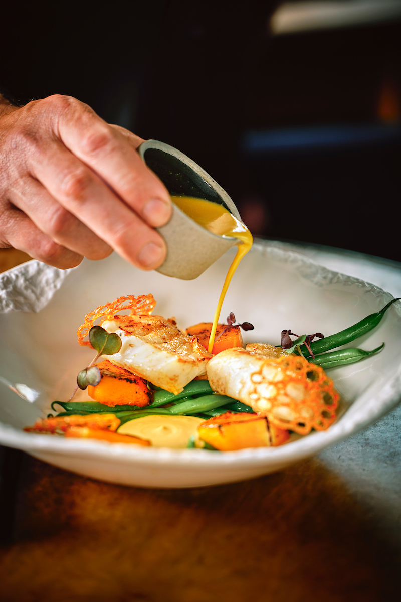 Colorful dish of fish with green beans, carrots, and sauce being poured, served at Apótek restaurant in Reykjavík, Iceland.