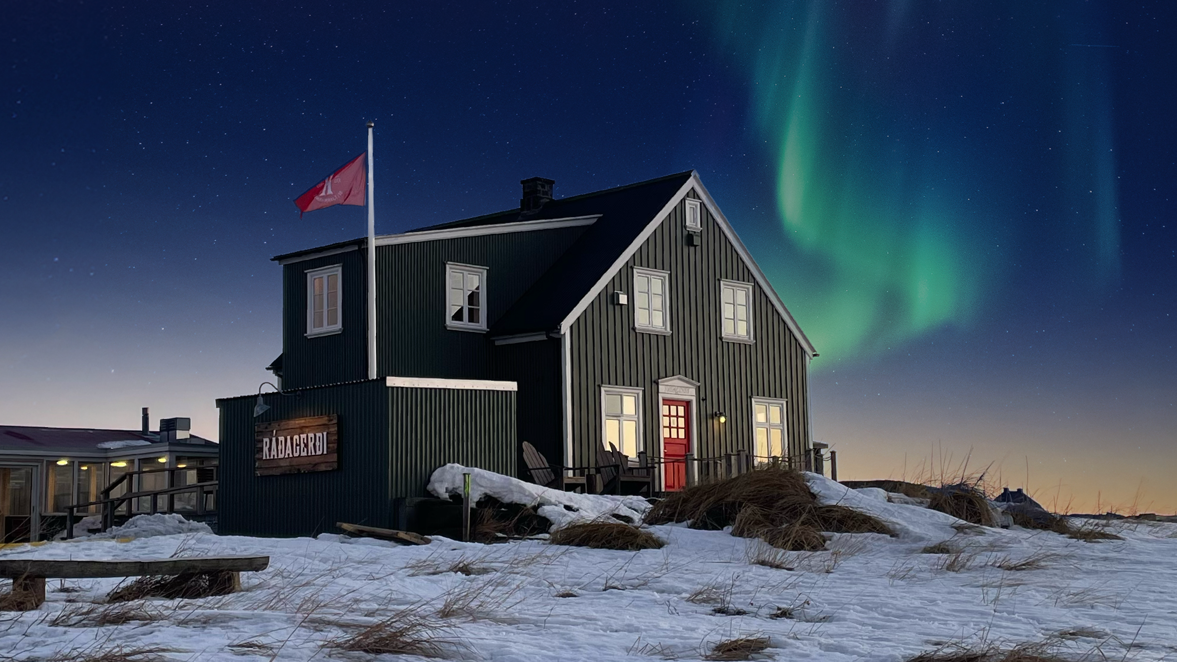 Ráðagerði restaurant in Seltjarnarnes, Iceland, a black wooden house lit up on a winter night with the northern lights visible in the sky.
