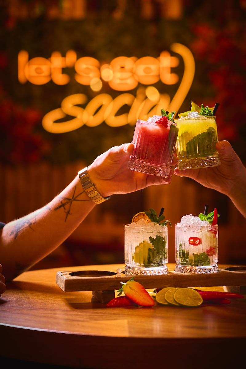 Colorful cocktails with fruit and mint served at Sushi Social in Iceland, with two people clinking glasses.