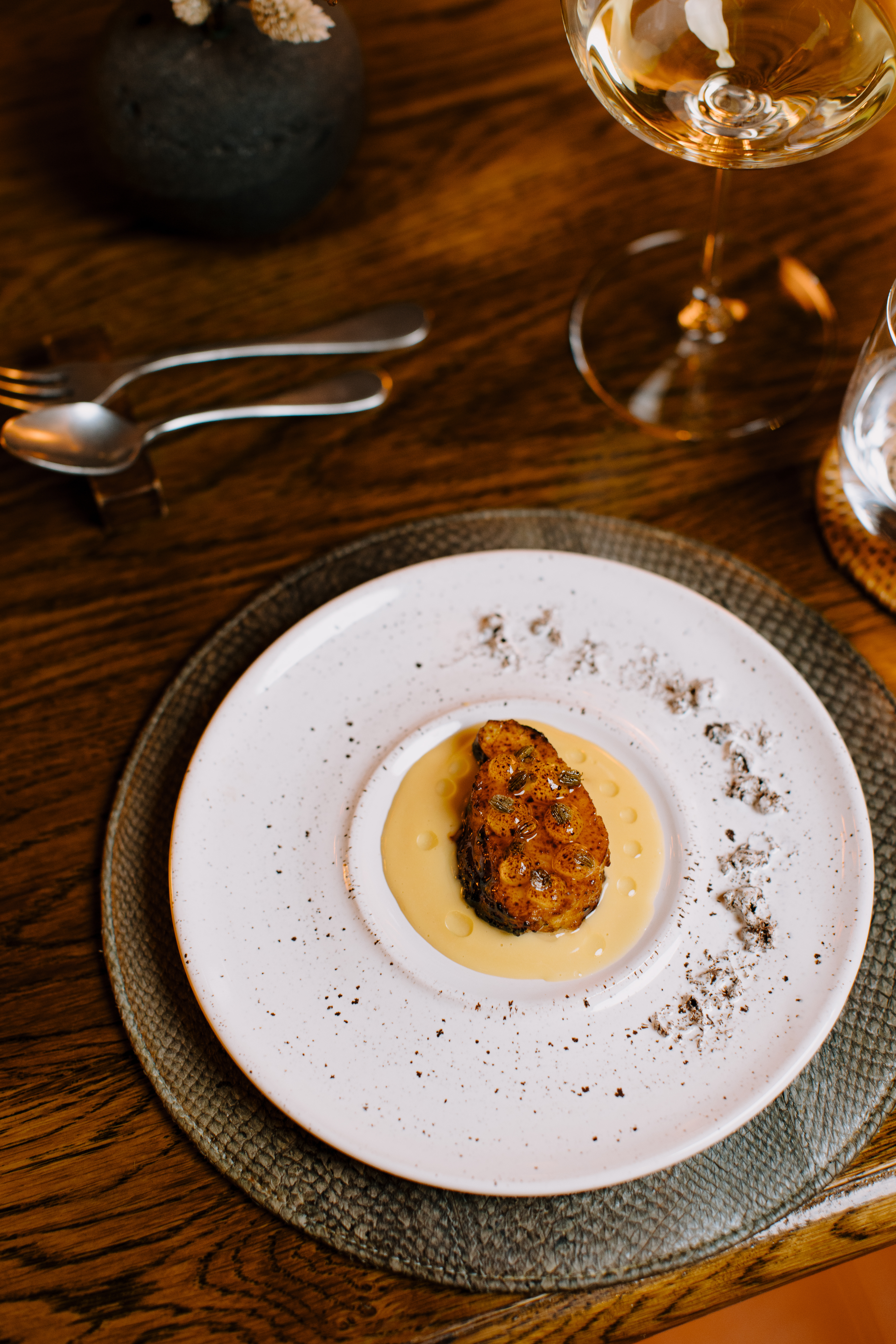 A plated tasting dish at ÓX, presented on layered ceramic plates with a glass of wine and cutlery set on a wooden table.