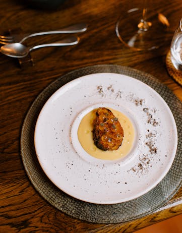 A plated tasting dish at ÓX, presented on layered ceramic plates with a glass of wine and cutlery set on a wooden table.