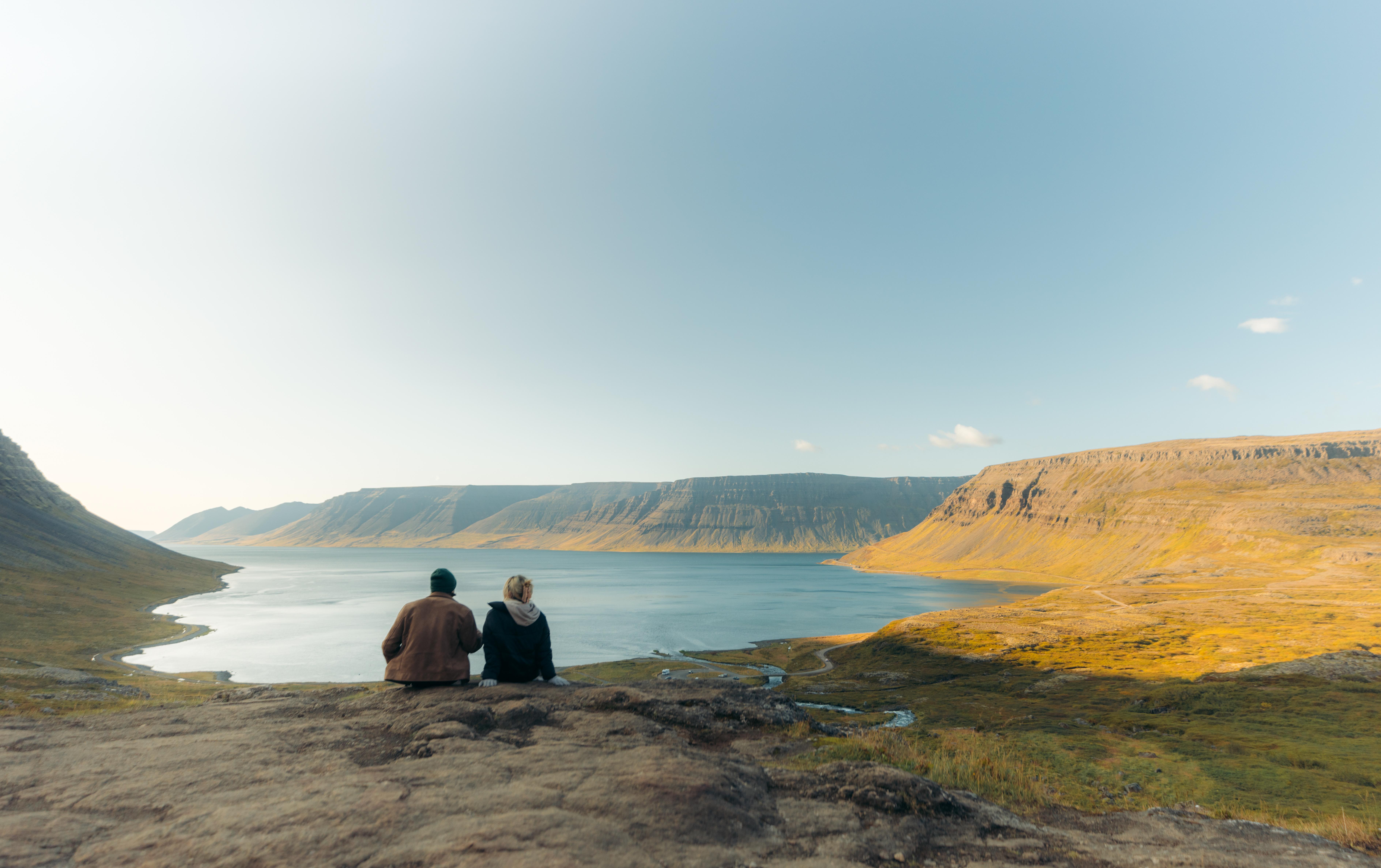 Two people sitting on a cliff overlooking Dynjandisvogur fjord in the Westfjords