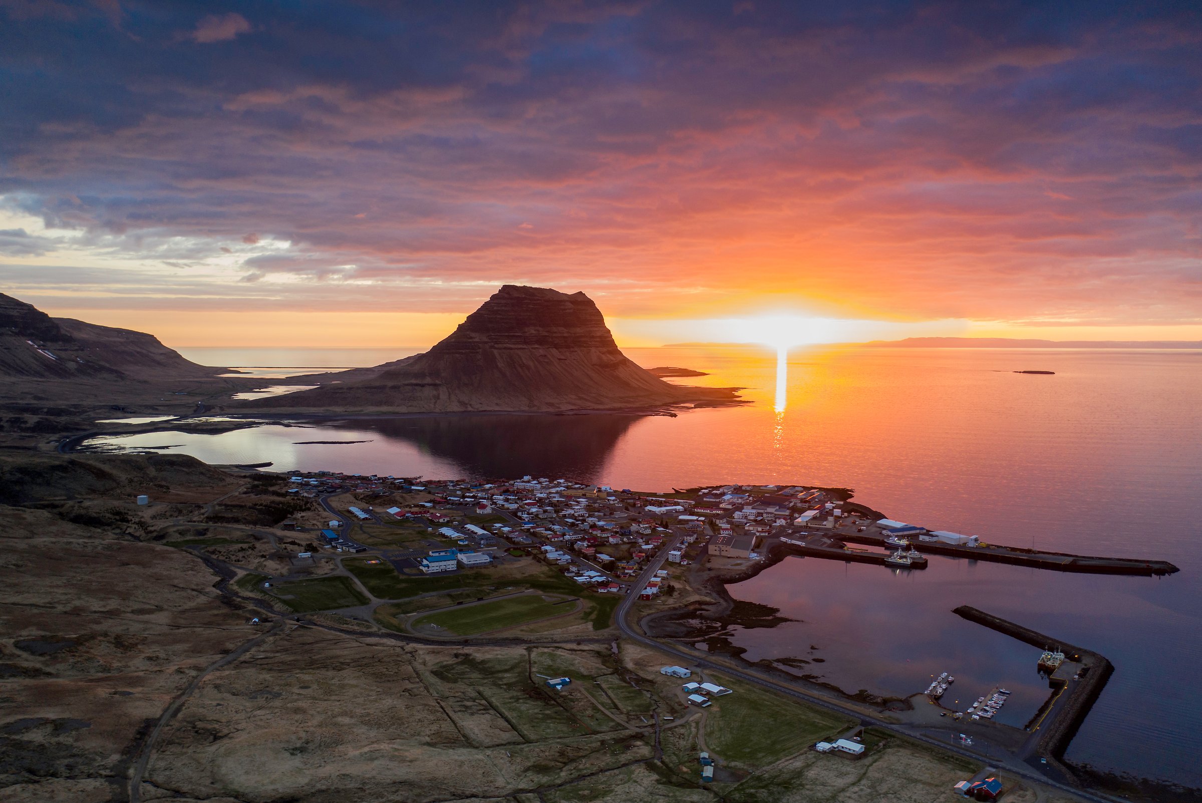 Kirkjufell mountain rising above Grundarfjörður at sunset, with the town and coastline in the foreground