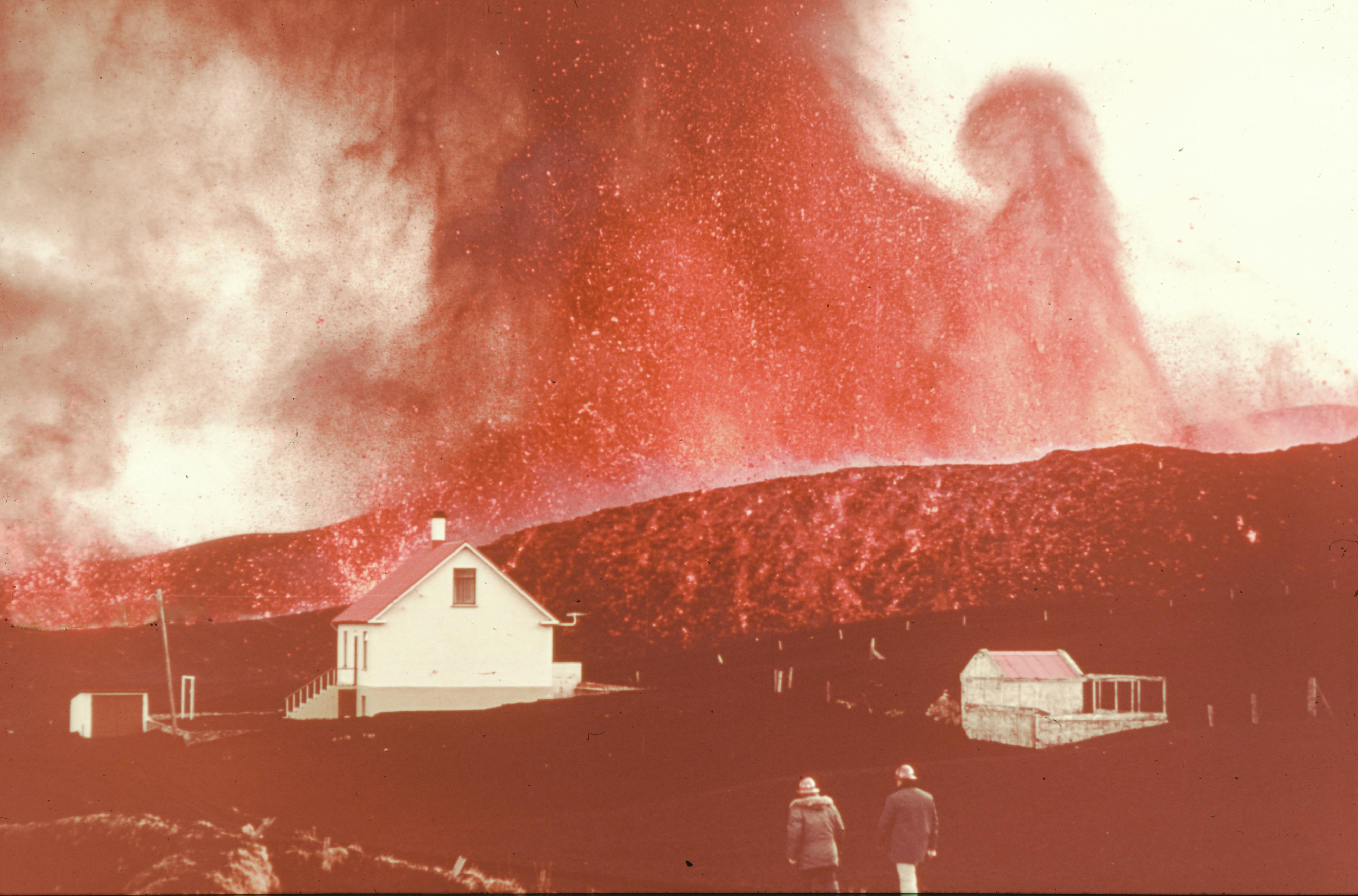Fierce volcano spewing glowing ash over a house as two men walk amidst the hazardous scene.