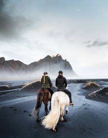A couple riding horses on a black sand beach