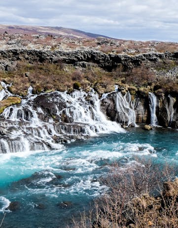 Series of spring waterfalls flowing from under a lava into a white-blue colored glacier river