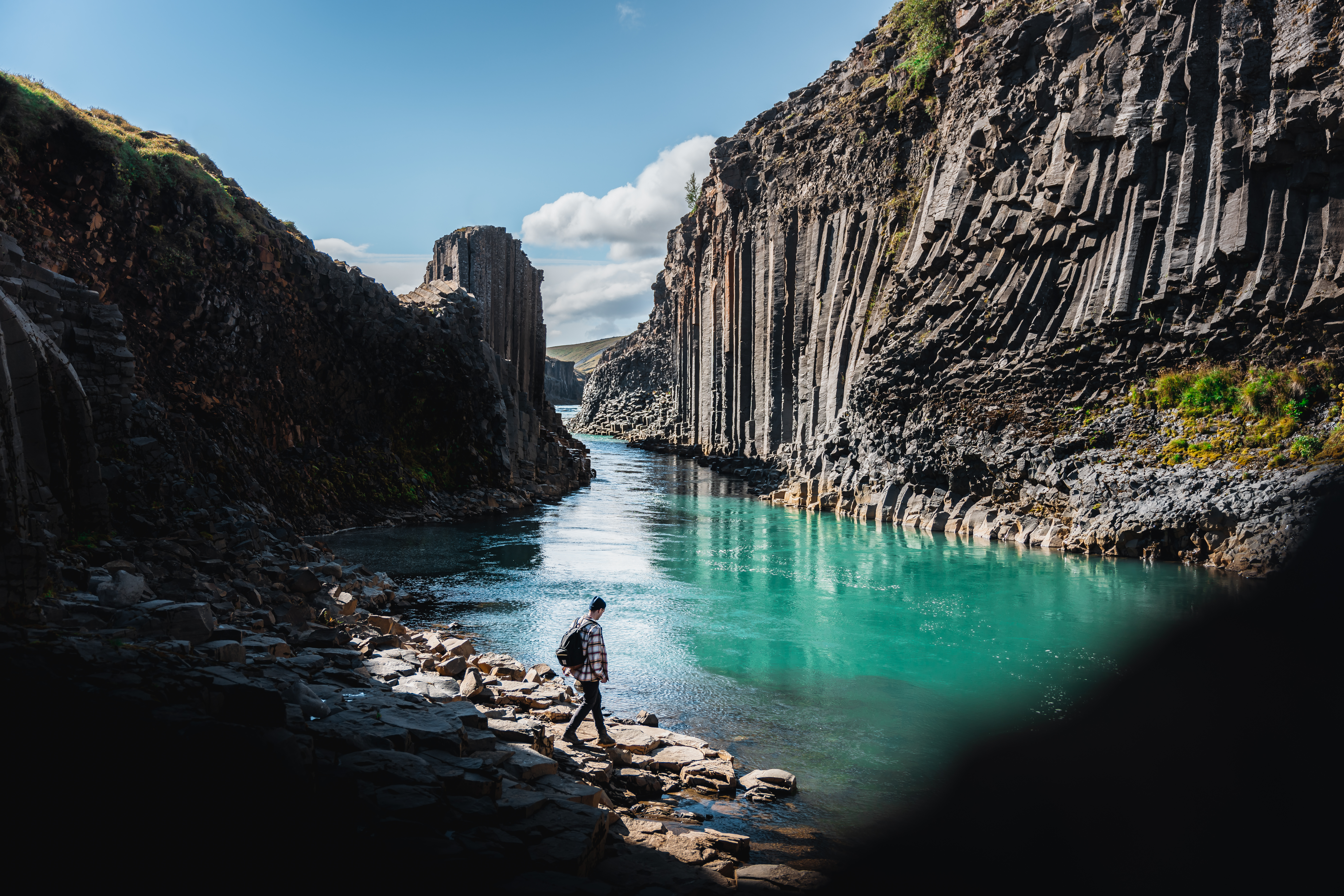 A person walking by Stuðlagil Canyon, with turquoise glacial waters flowing between steep basalt cliffs in East Iceland.