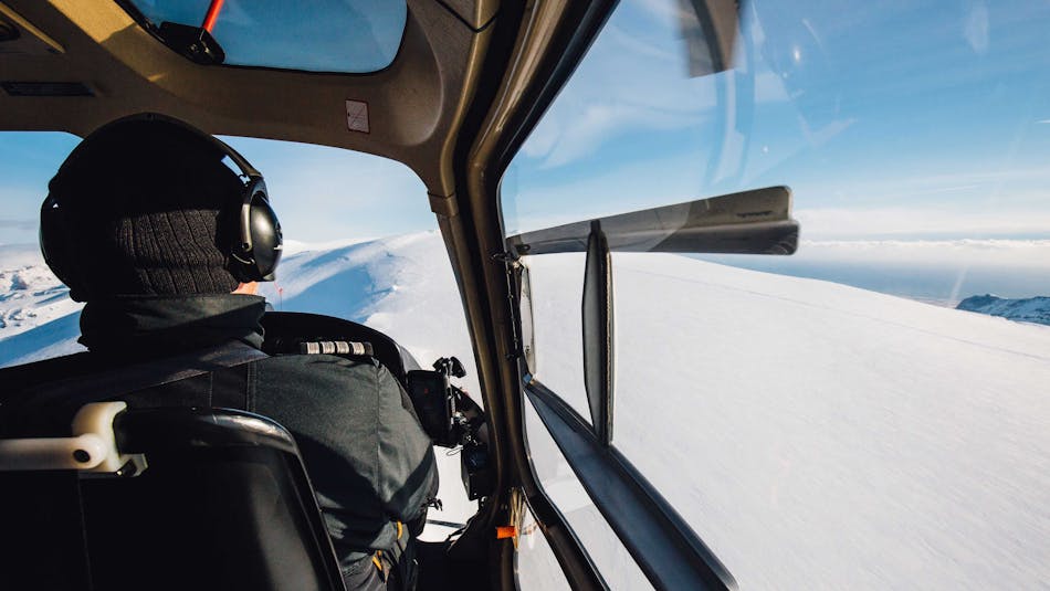 A pilot flying a helicopter over snowy mountains