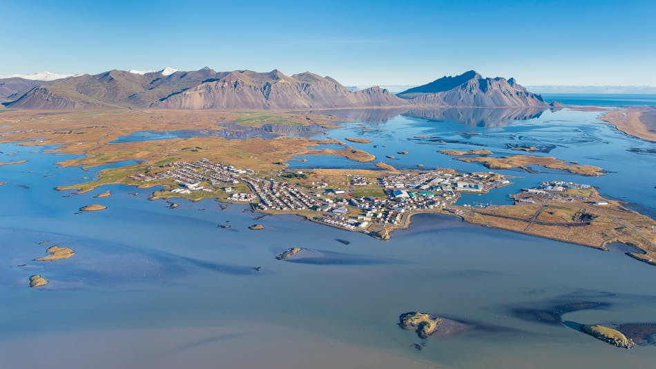 An aerial photograph of a small town enveloped by the ocean and a river and a mountain range in the backdrop.
