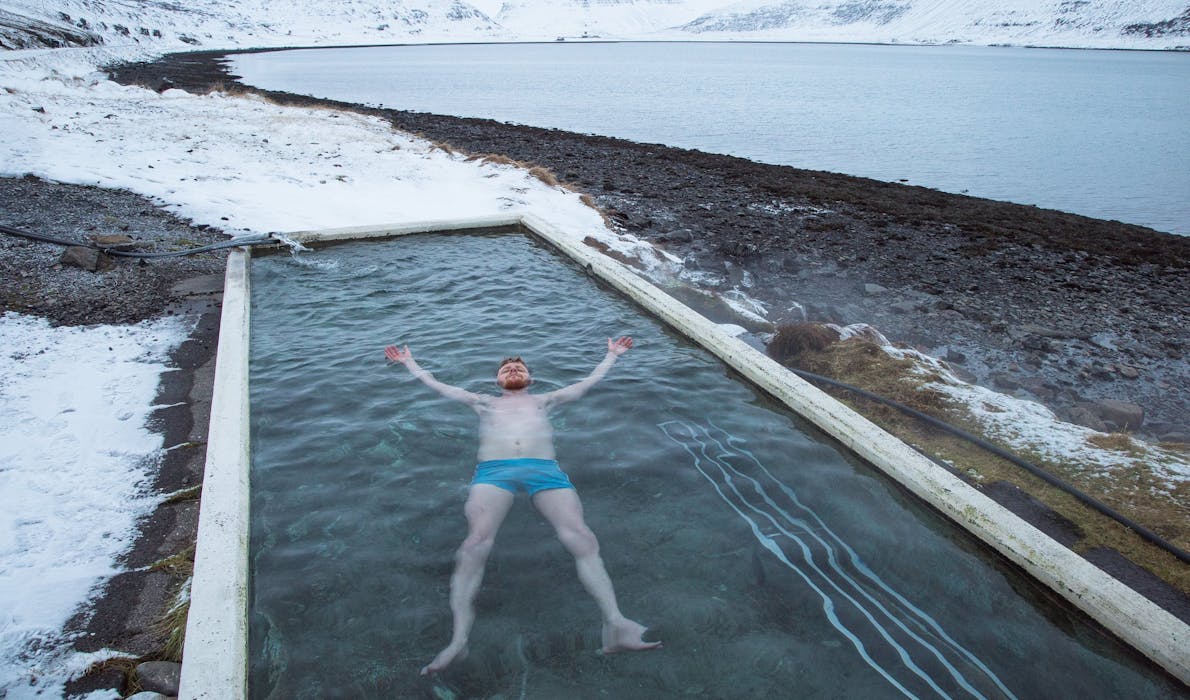 Man in blue bathing shorts lying in a hotwater pool surrounded only by snowy mountains