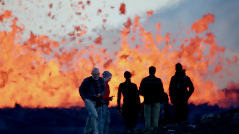 People standing in front of an erupting volcano