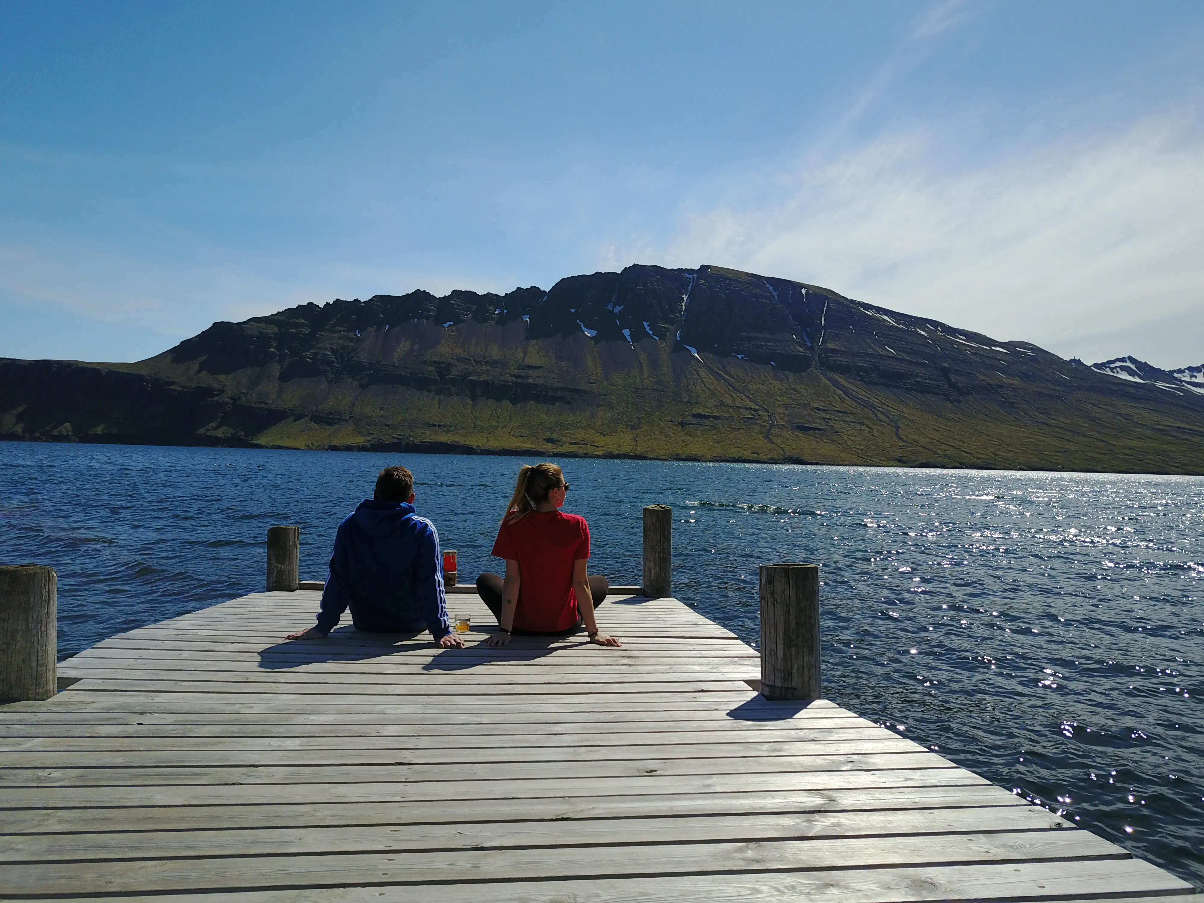 A couple sitting on the end of a dock looking out to sea