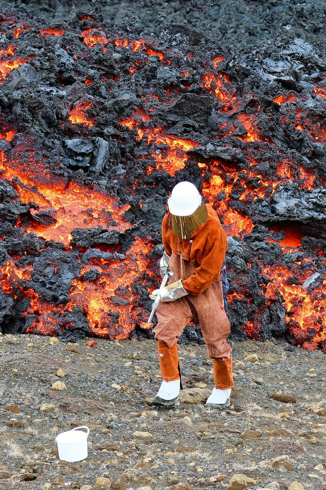 A person in a thermal suit collecting samples from flowing lava