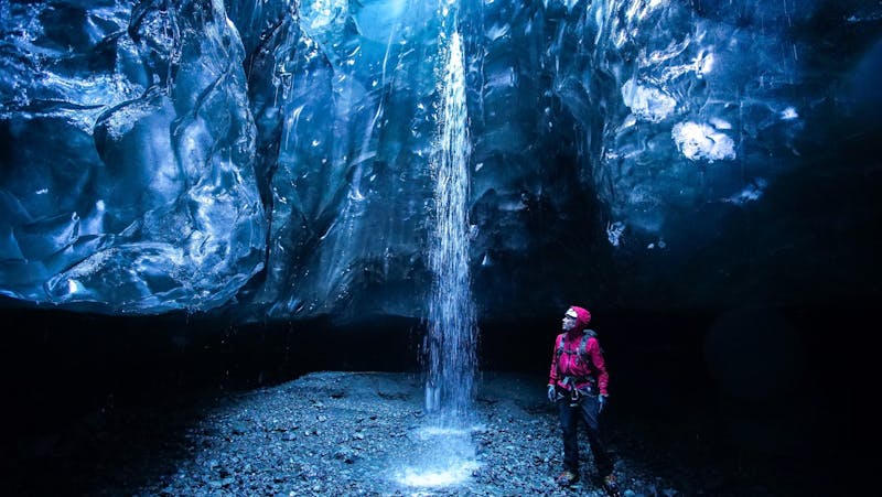 A man standing by a small waterfall in an ice cave