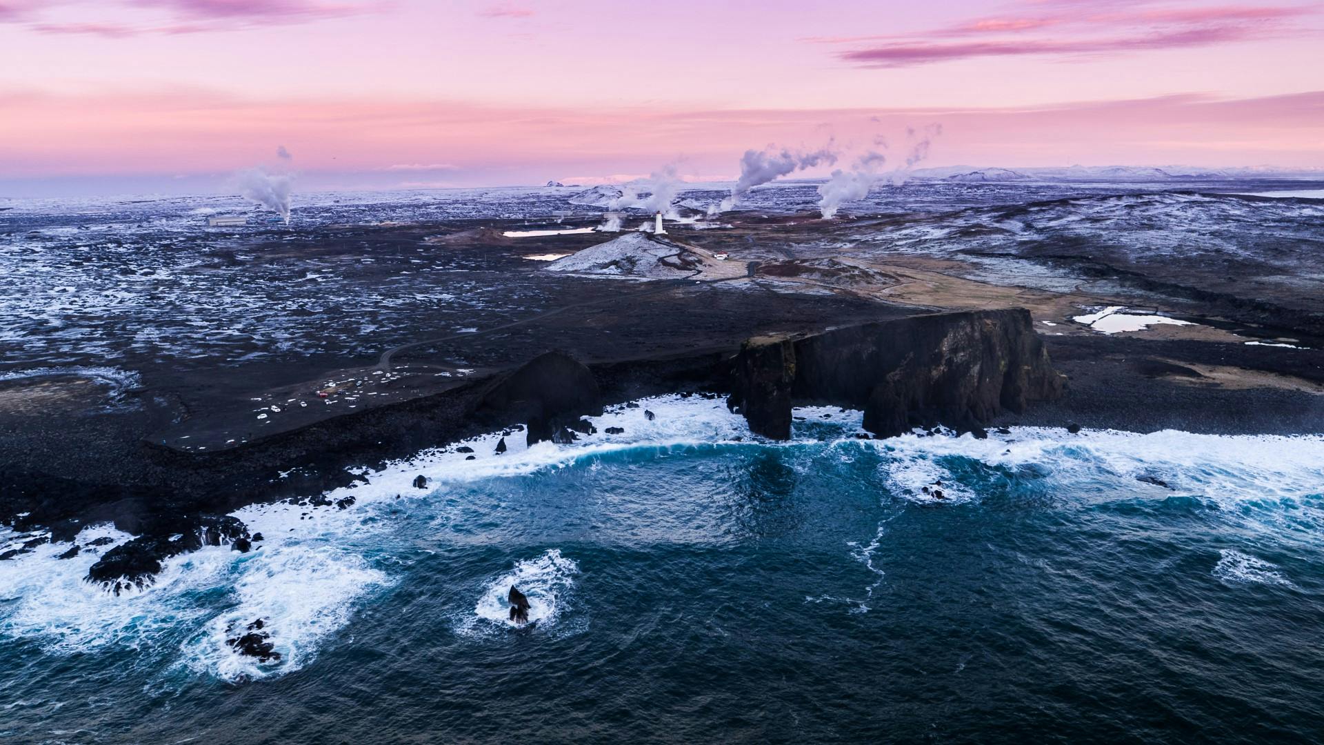 An aerial view of a rugged coastline with steam rising from a power plant nearby