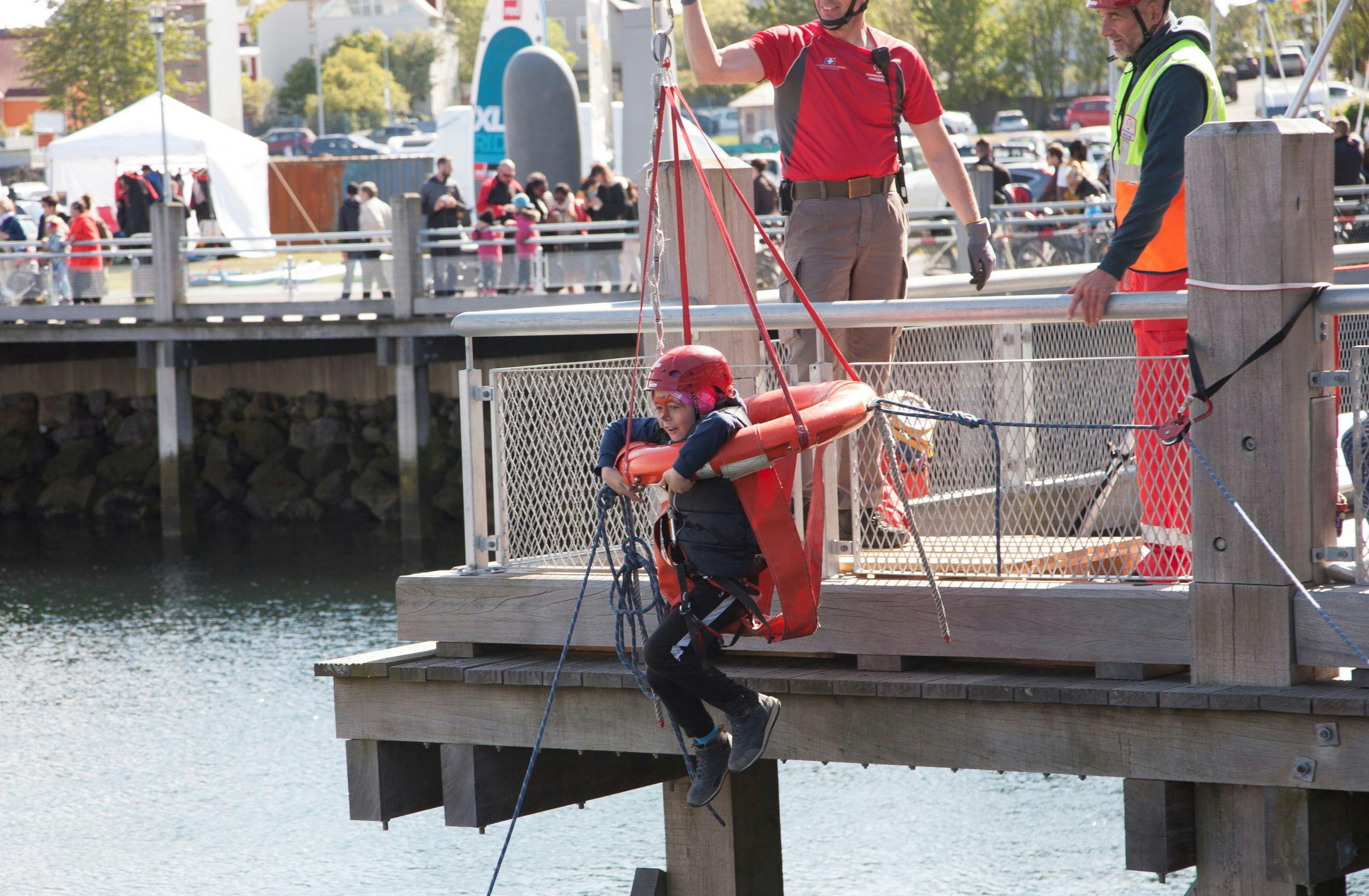 A child wearing a helmet, hanging in a rescue ring above the water in Reykjavík harbour as part of the Fisherman's Day festivities.