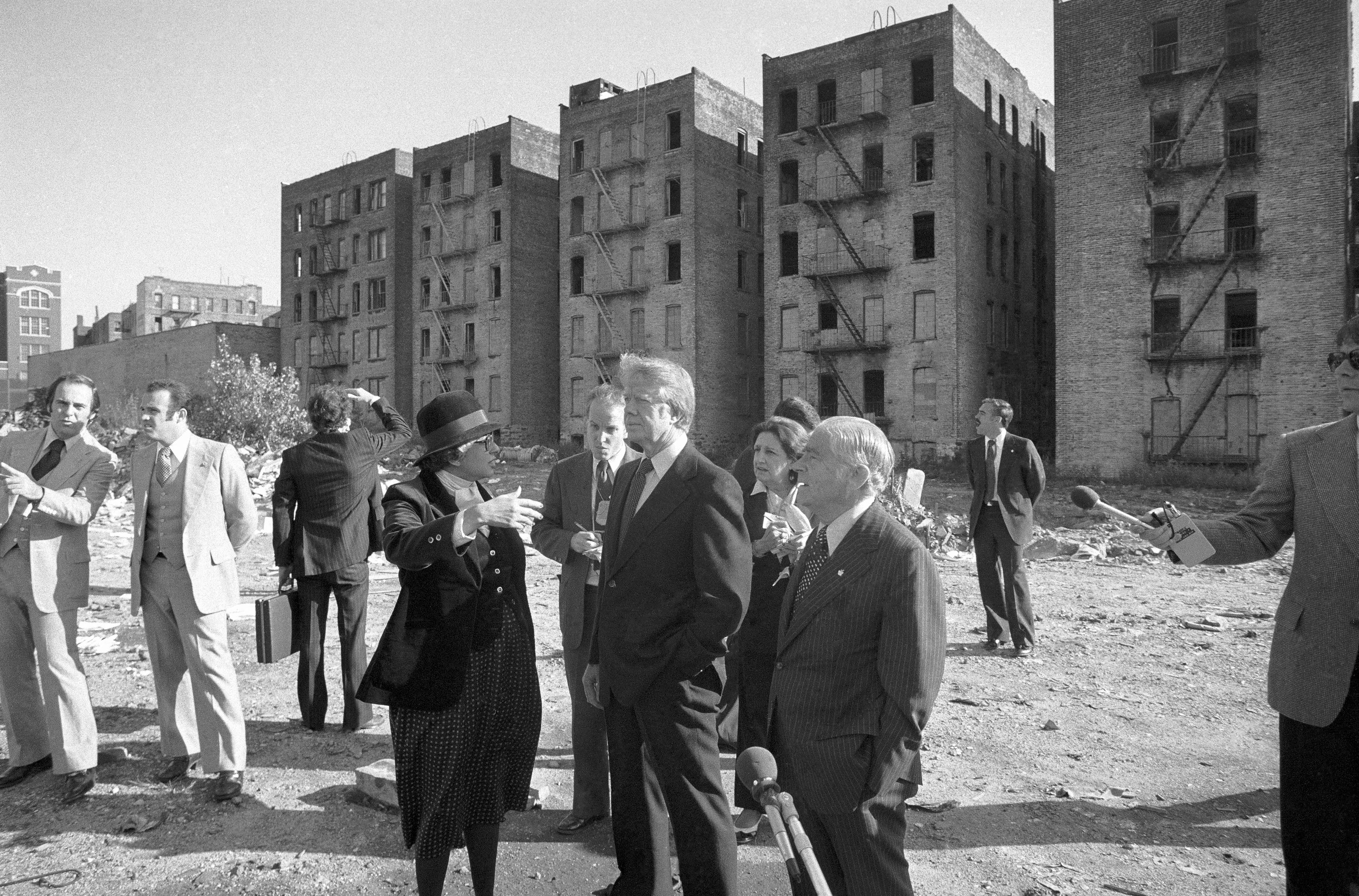 President Jimmy Carter stands in front of a row of burned out apartment buildings in the South Bronx, accompanied by U.S. Secretary of Housing and Development Patricia Harris and New York City Mayor Abe Beame.