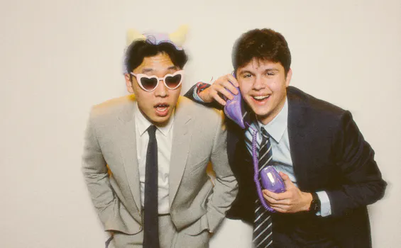 Two friends in suits with sunglasses pose for a photo.