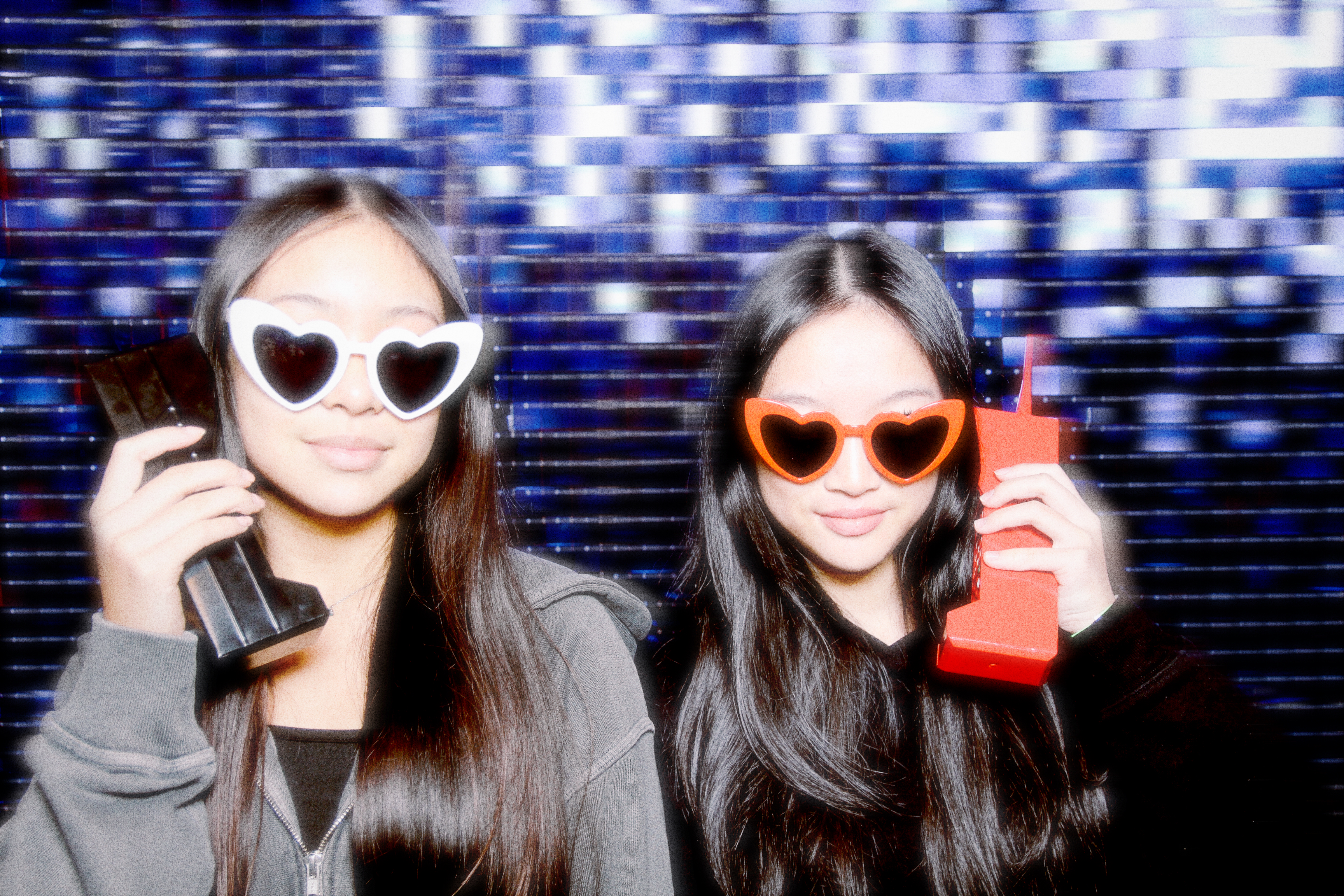 Two young women posing with phones in front of the photo booth