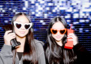 Two young women posing with phones in front of the photo booth