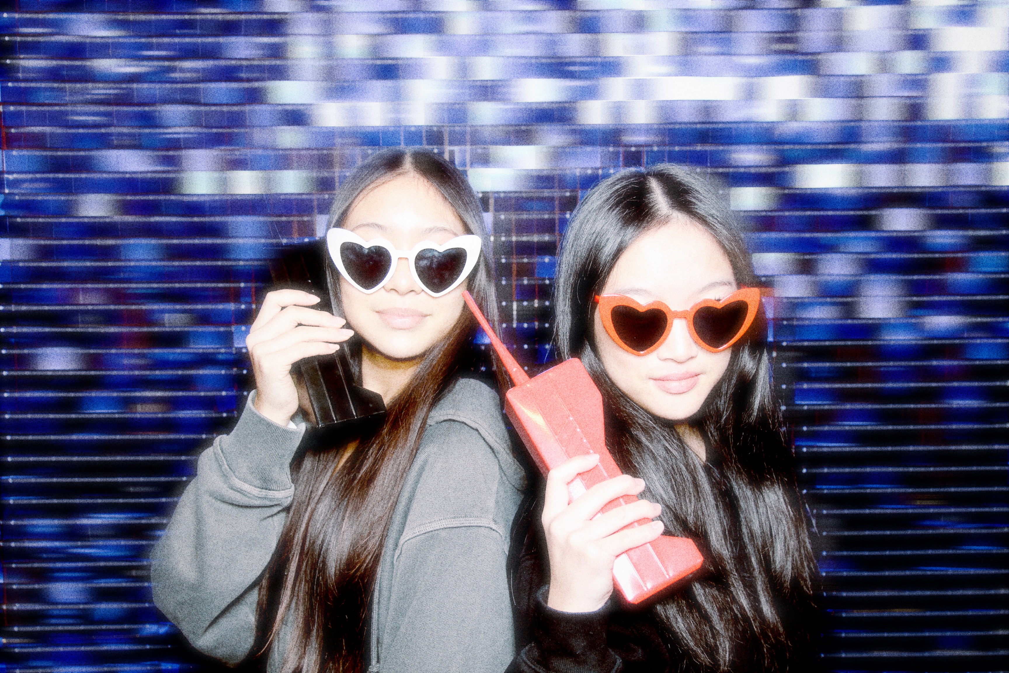 Two young women posing with phones in front of the photo booth