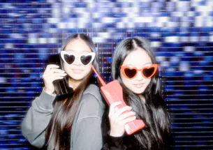 Two young women posing with phones in front of the photo booth