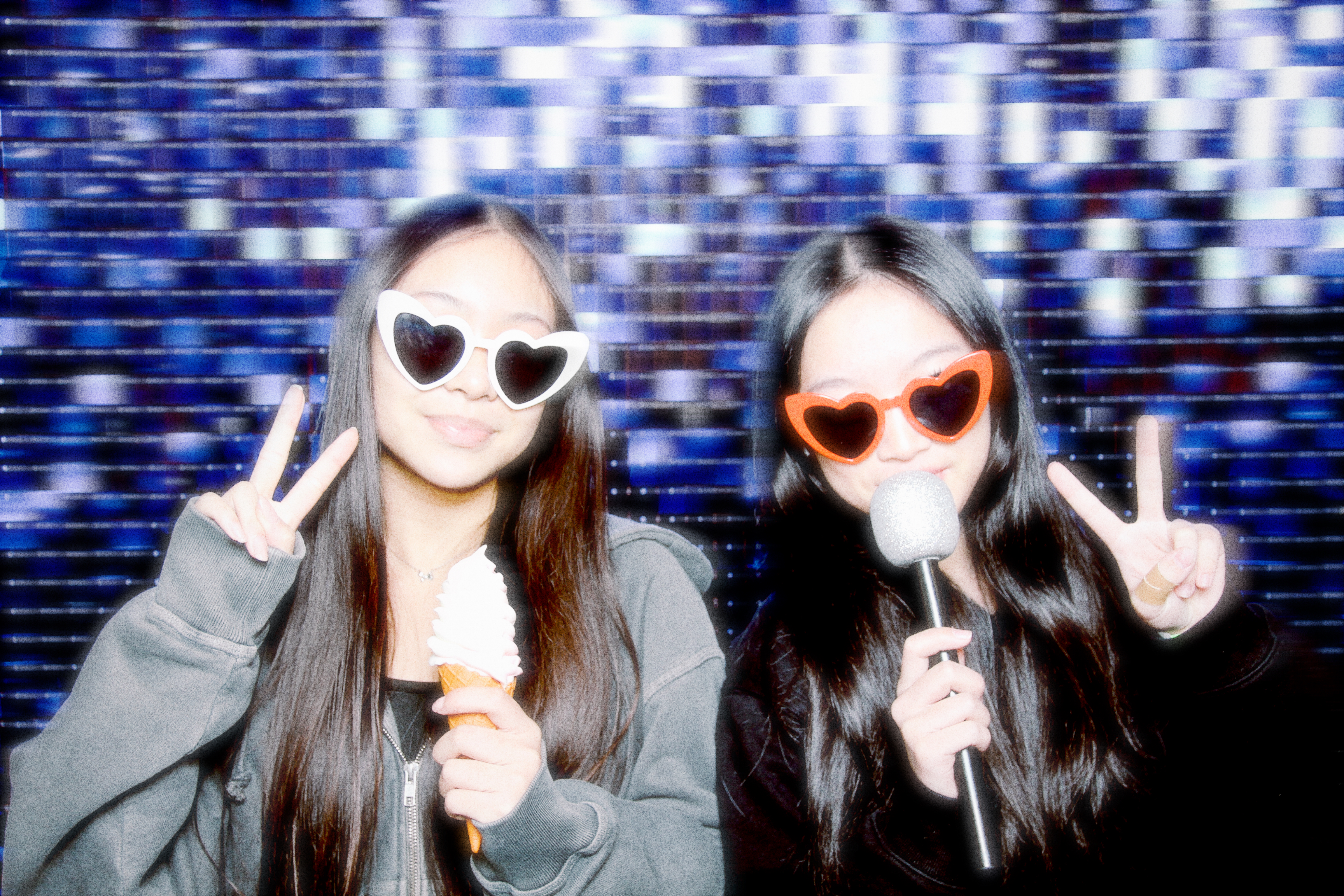 Two young women posing with microphones in front of the photo booth
